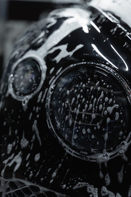 A detailed close-up of a car headlight covered with soap suds during a wash.
